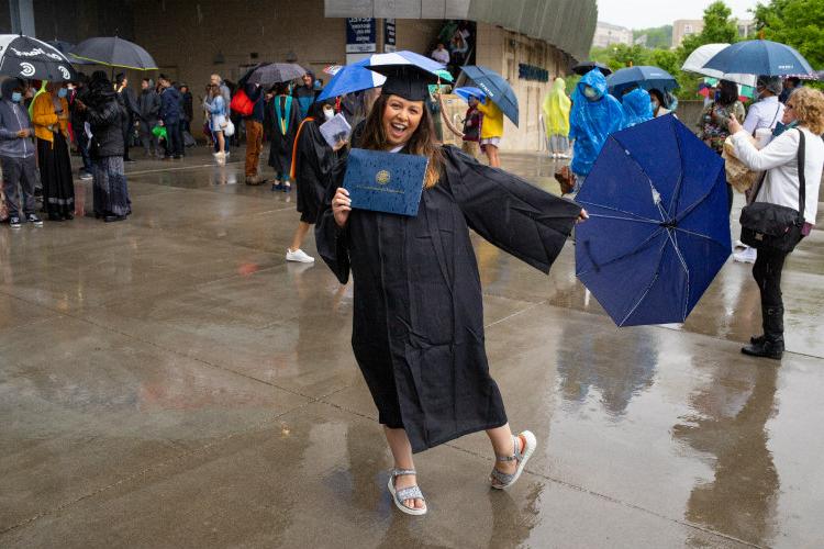 Female in regalia with diploma and umbrella in the rain