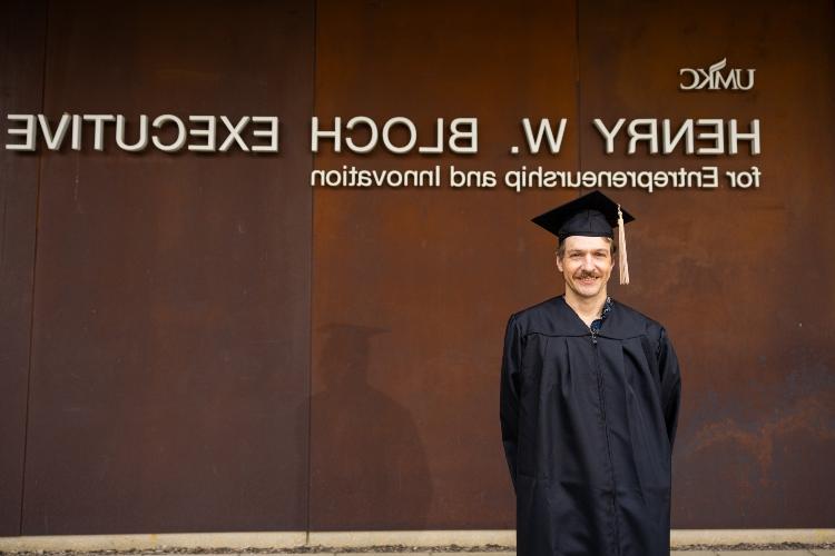 Cody Truitt wearing graduation regalia in front of Bloch Eexecutive Hall.